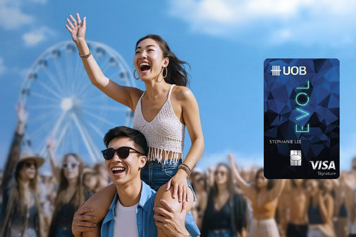 Smiling couple enjoying an outdoor festival beside a UOB EVOL Visa card